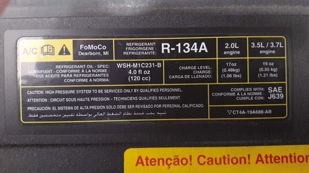 Foto de uma etiqueta - Ford Edge 2011 - indicando fluido refrigerante R-134a, sua quantidade de fluido específica para cada tipo de motor, e seu tipo de óleo lubrificante e quantidade total específica